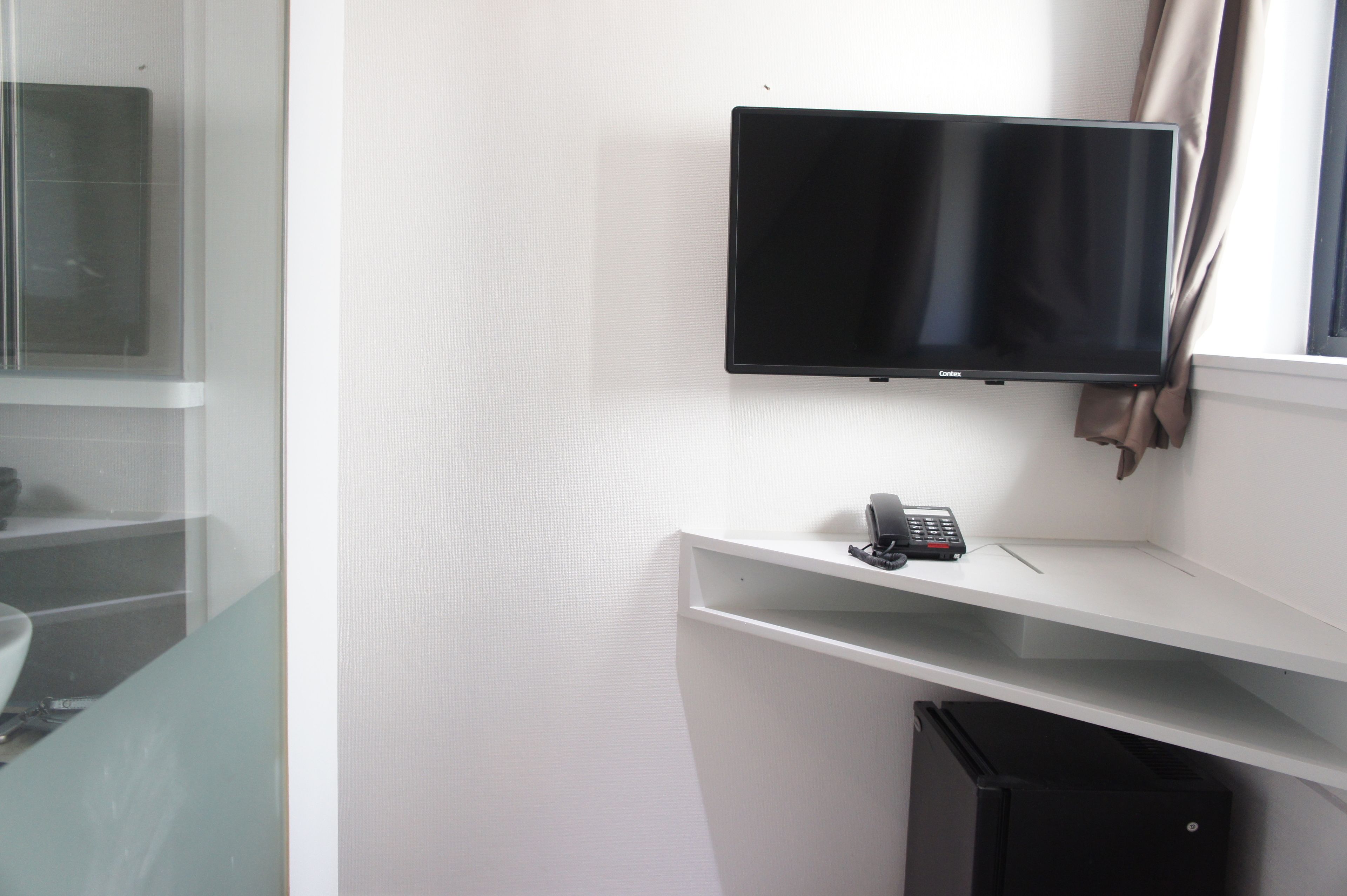 A hotel room with a flat-screen TV mounted on the wall, a telephone, and a small desk.