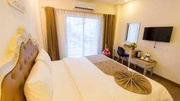 A hotel room with a bed, a desk, a chair, a TV, and an air conditioning unit.