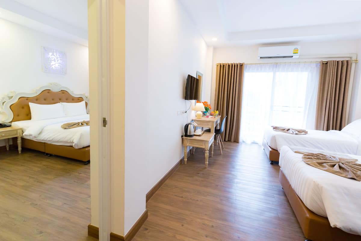 A hotel room with two beds, a desk with a chair, a TV, and an air conditioning unit.