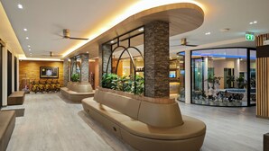 A modern lobby with a curved seating area, a reception desk, and a glass partition with plants. - Hi Chiangrai Hotel (Chiang Rai)