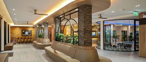 Een moderne lobby met een gebogen zithoek, een receptiebalie en een glazen scheidingswand met planten.