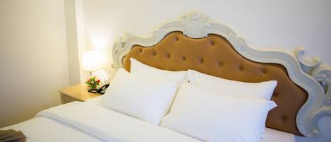 Una cama bien hecha con sábanas blancas, una mesita de noche de madera con una lámpara, y un adorno decorativo sobre la cama.