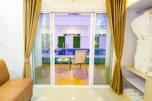 A hotel room with a sliding glass door leading to a balcony with a pool, a chair, and a table with a fruit bowl.