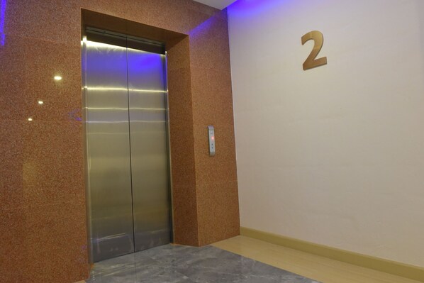 A modern elevator with a metallic finish, a wall-mounted number '2' sign, and a marble floor.