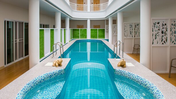 A multi-level indoor swimming pool with a central circular section, surrounded by balconies and a skylight. - Hi Chiangrai Hotel (Chiang Rai)