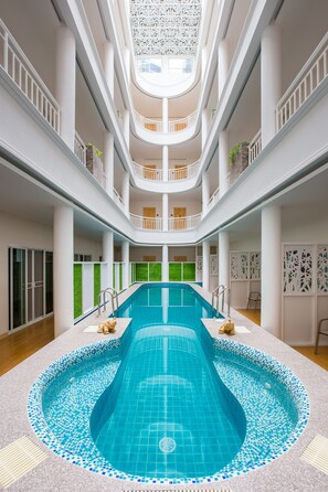 A multi-level indoor swimming pool with a central circular section, surrounded by balconies and a skylight.