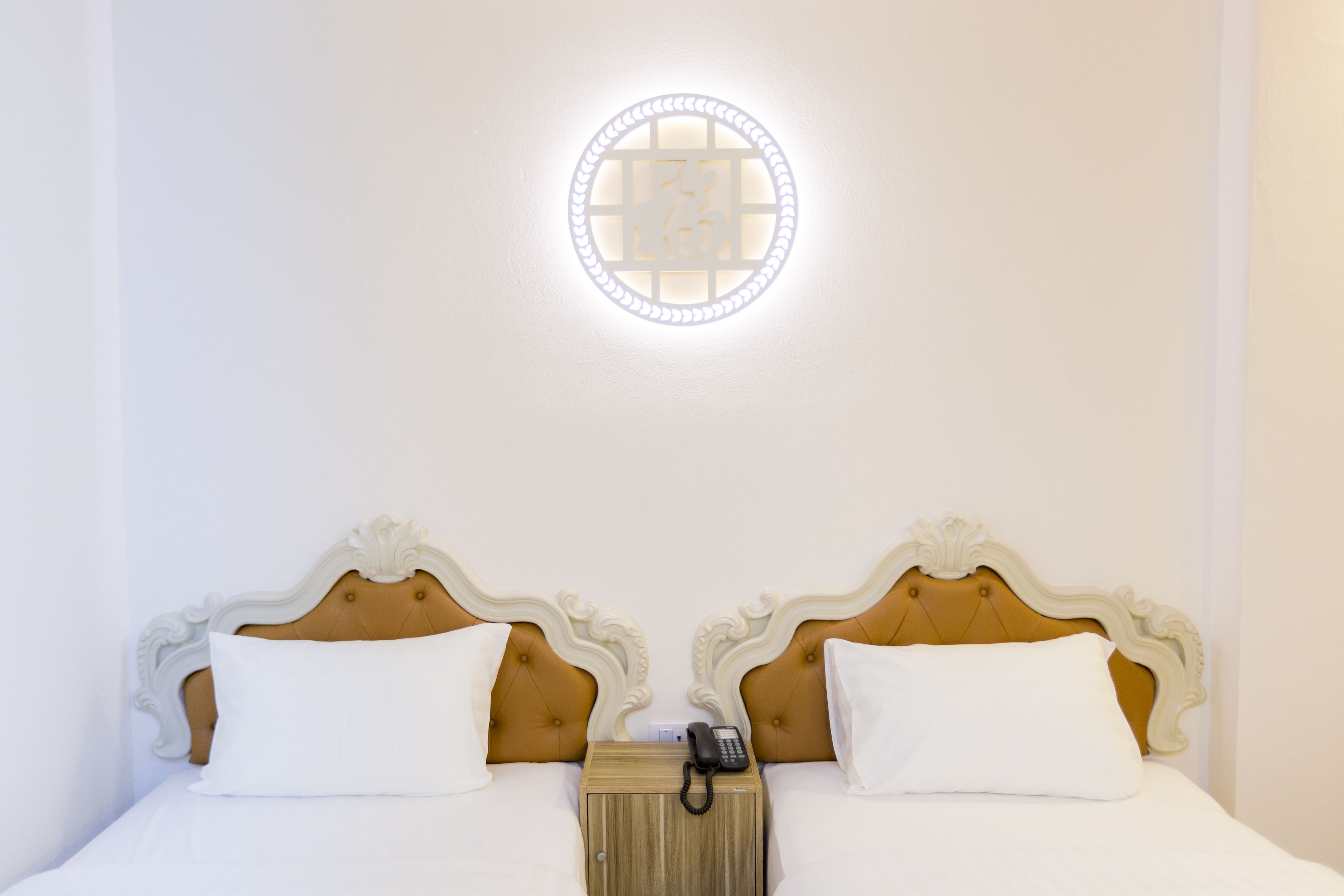 A double bed with white linens, a wooden nightstand with a telephone, and a wall-mounted light fixture.