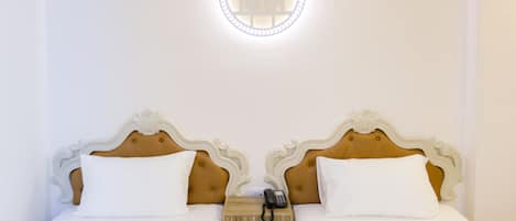 A double bed with white linens, a wooden nightstand with a telephone, and a wall-mounted light fixture.