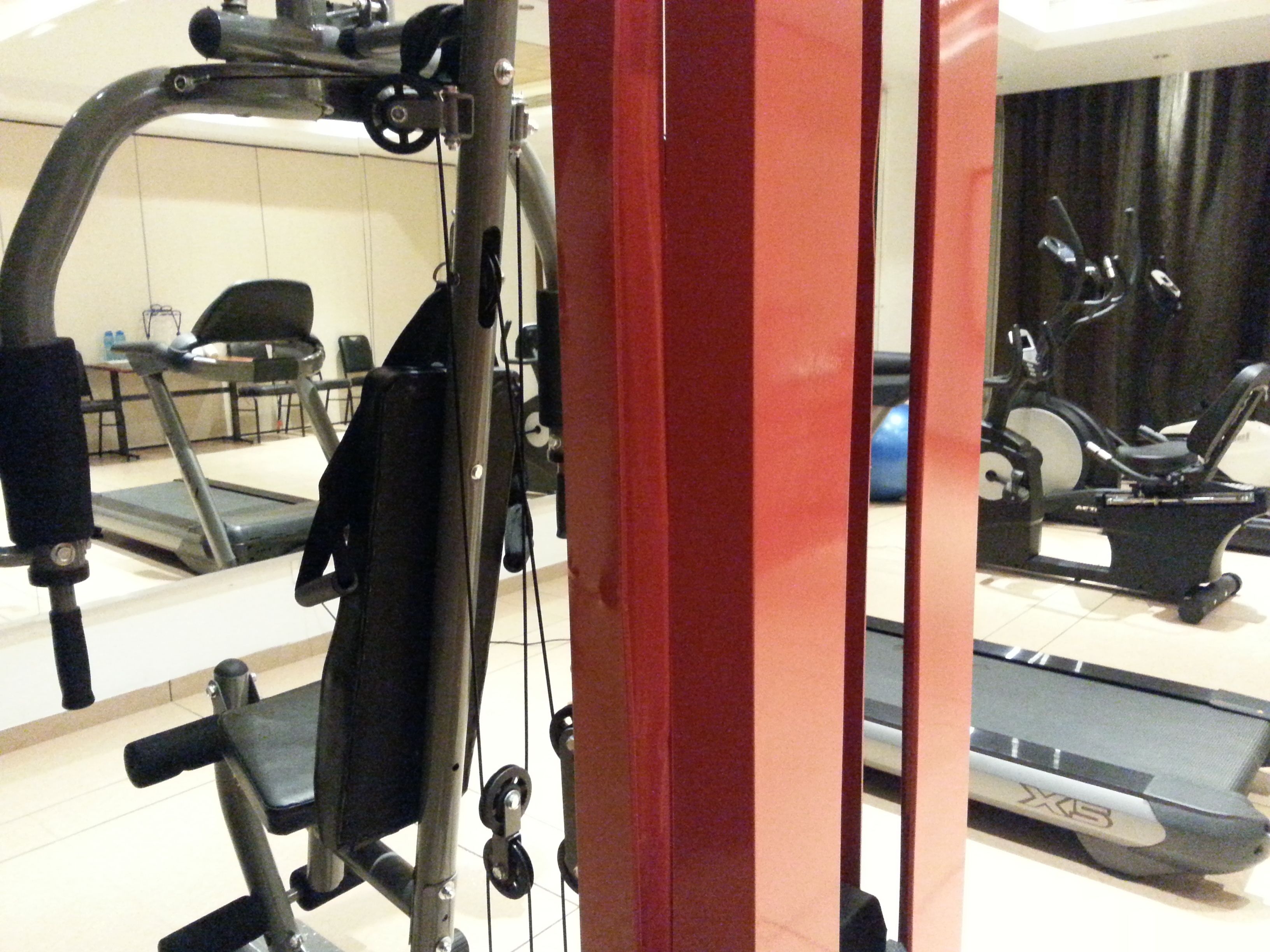 A gym with exercise equipment, a treadmill, and a mirror reflecting the room.