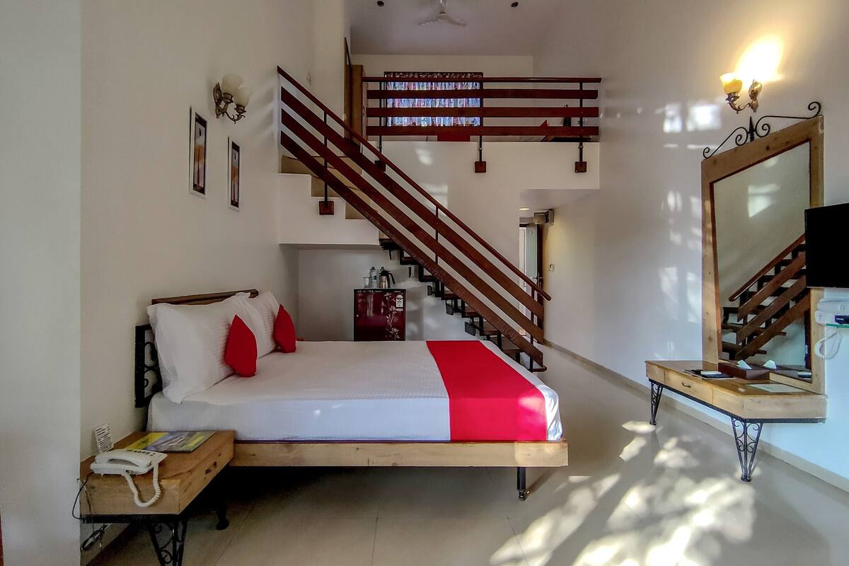 A bedroom with a bed, a wooden nightstand, a desk, a mirror, a staircase, and a ceiling fan.