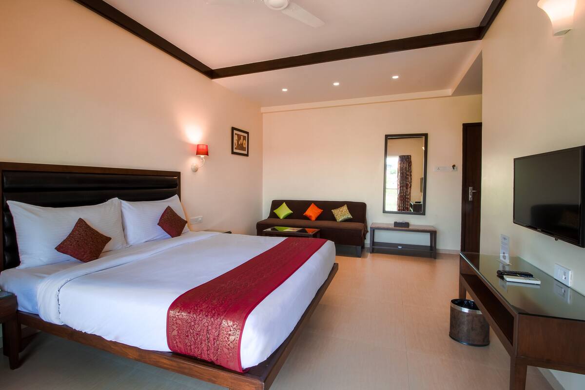 A hotel room with a large bed, a TV, a desk, and a sofa.