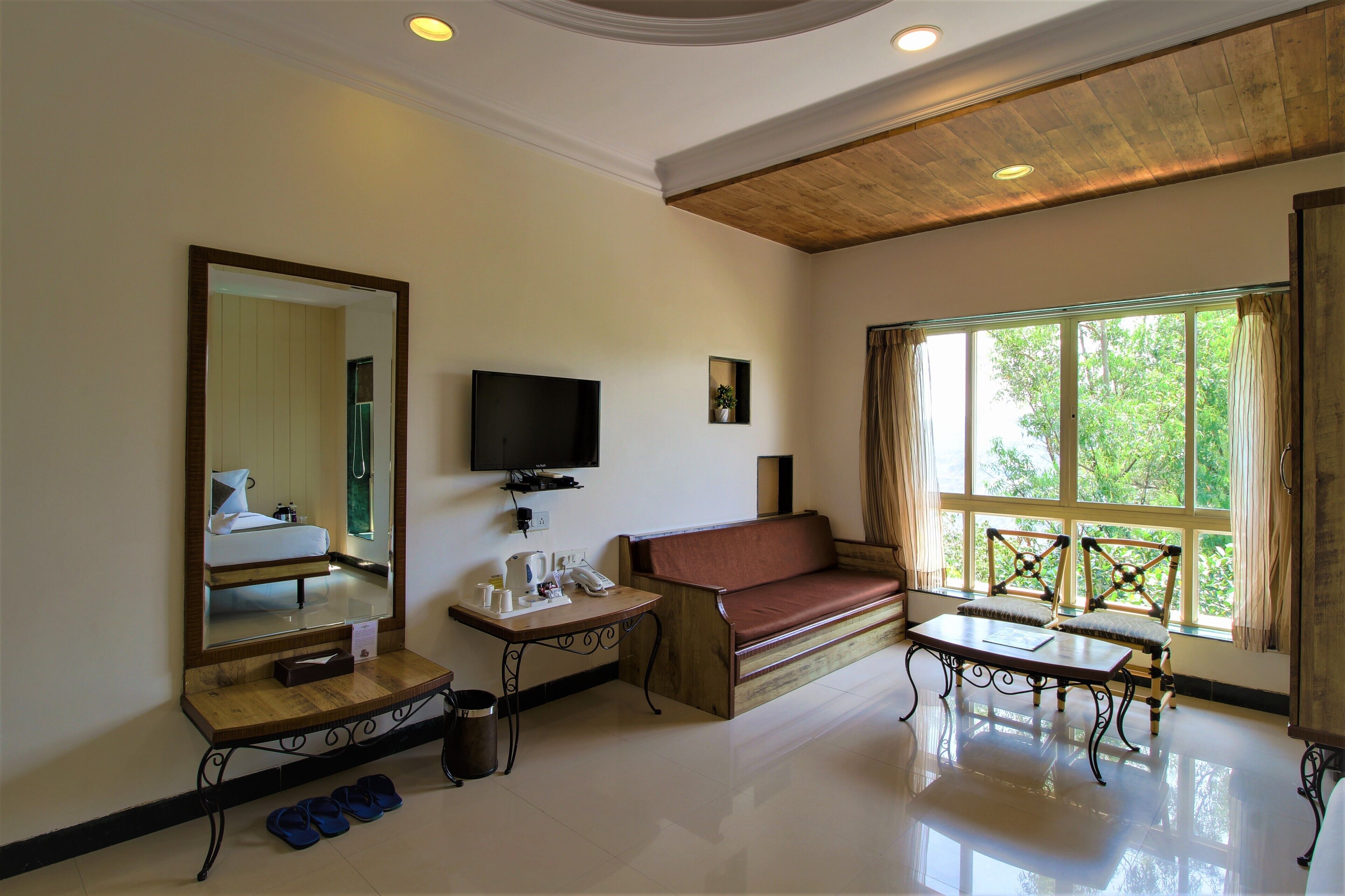 A room with a wooden ceiling, a sofa, a TV, a window with curtains, and a mirror.