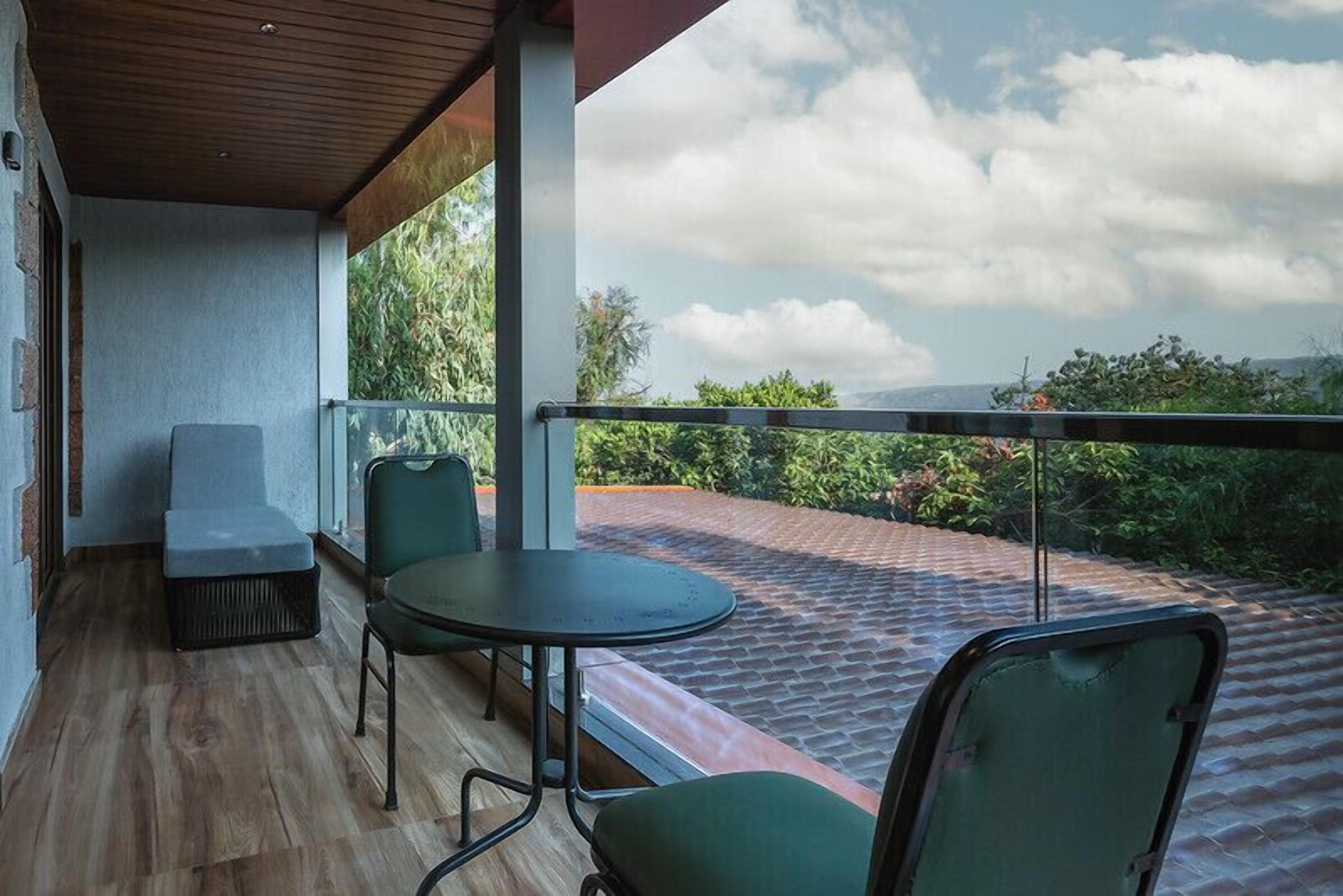 A balcony with a table and chairs, a view of greenery and distant hills, and a wooden floor.