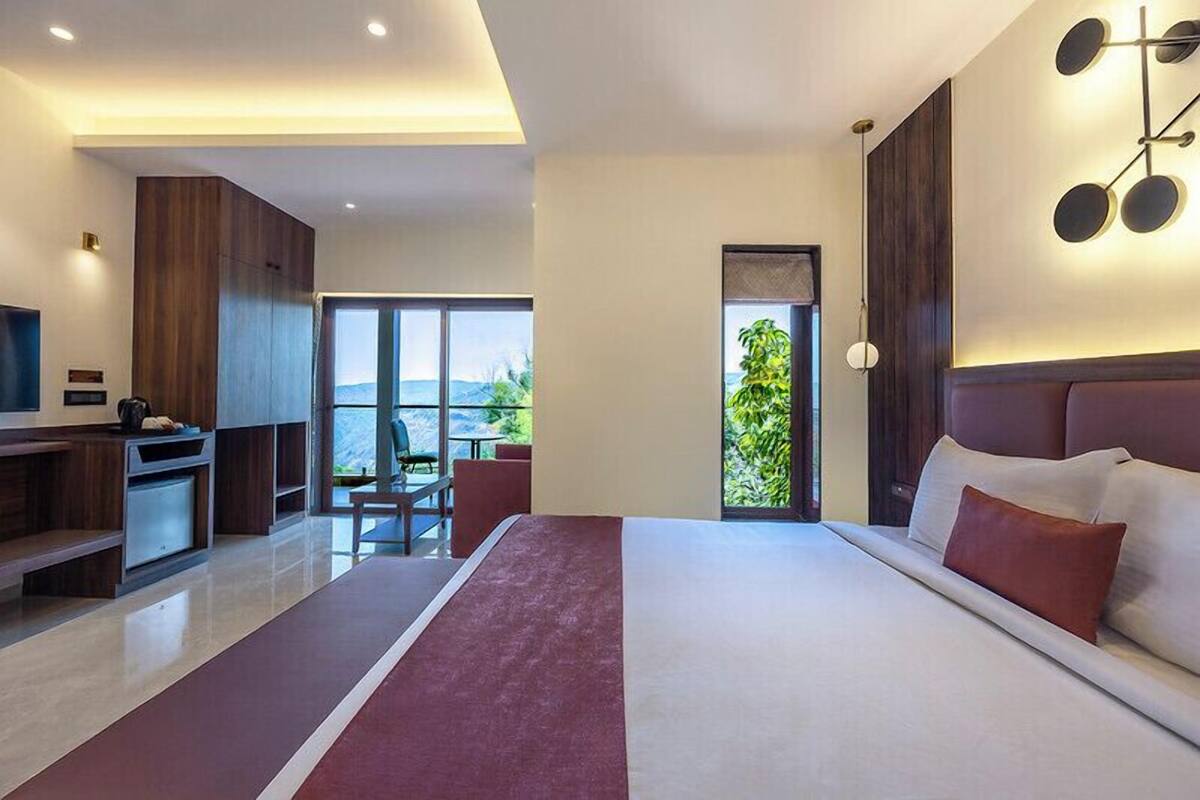 A modern hotel room with a large bed, a TV, a desk, and a view of the outdoors.