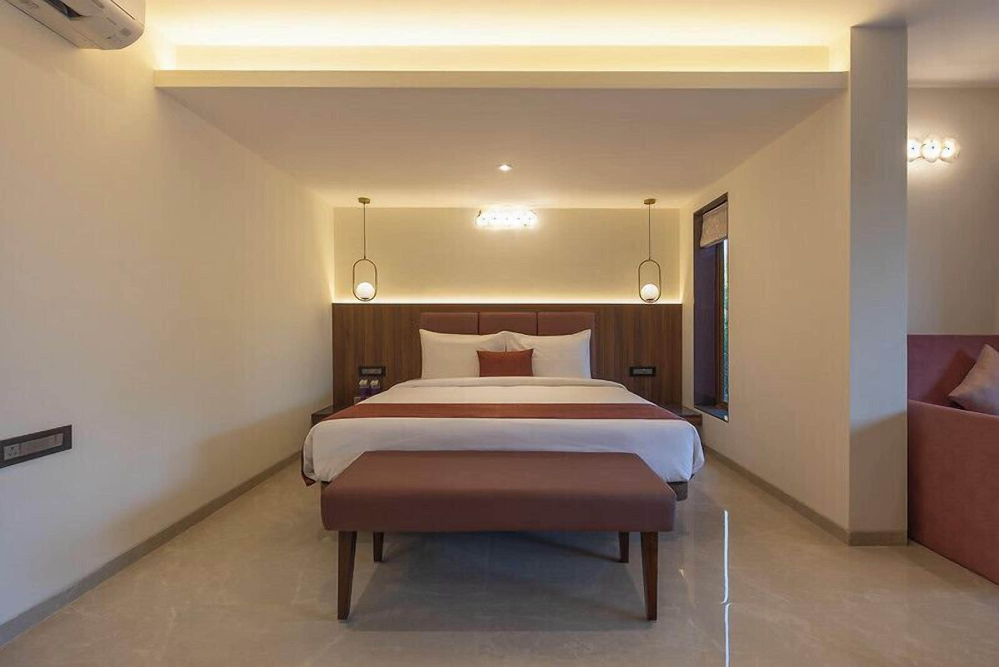 Une chambre d’hôtel moderne avec un grand lit, des tables de chevet, un banc et une grande fenêtre.