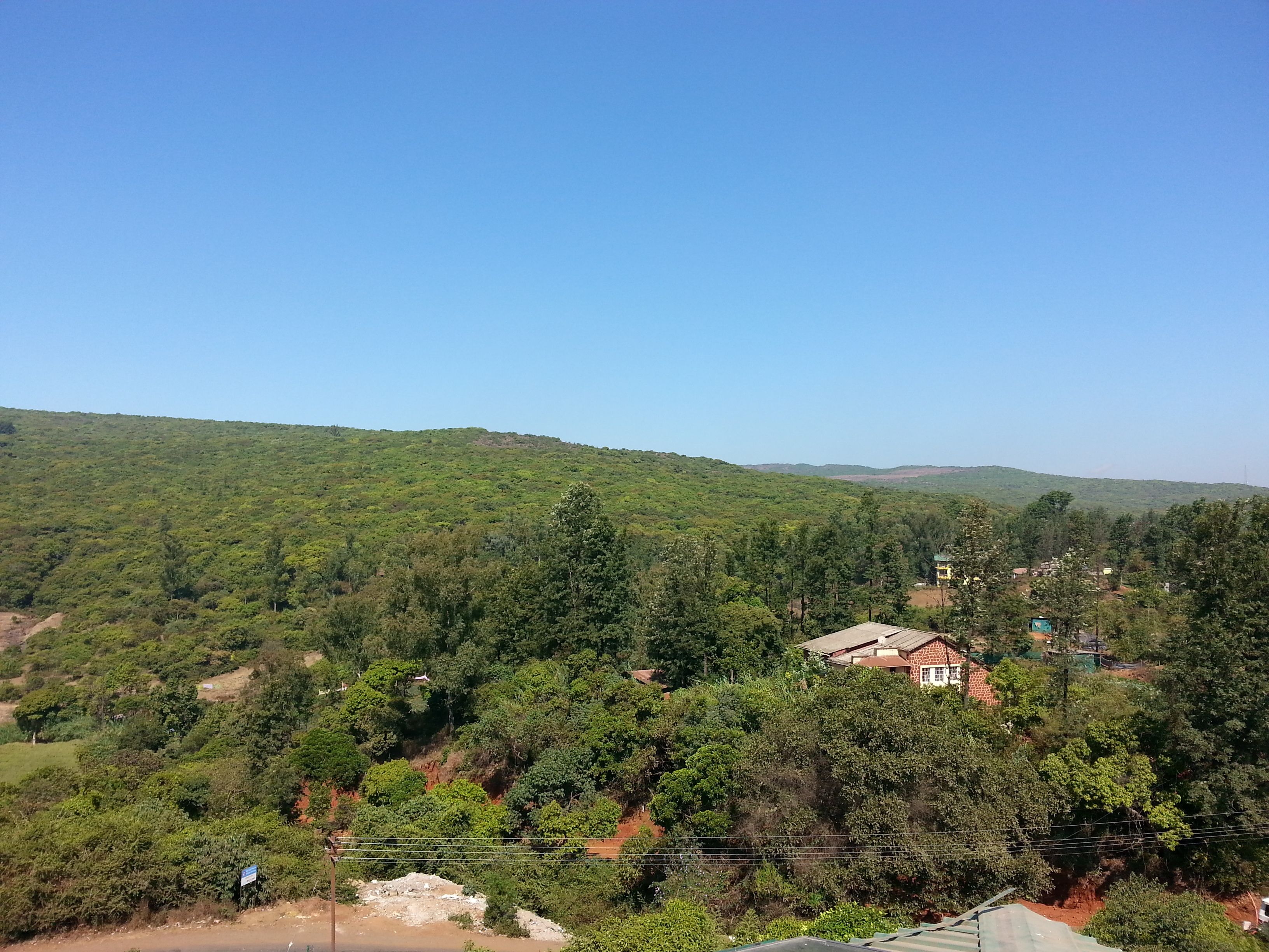 Un paisaje rural con una casa rodeada de abundante vegetación y colinas al fondo.