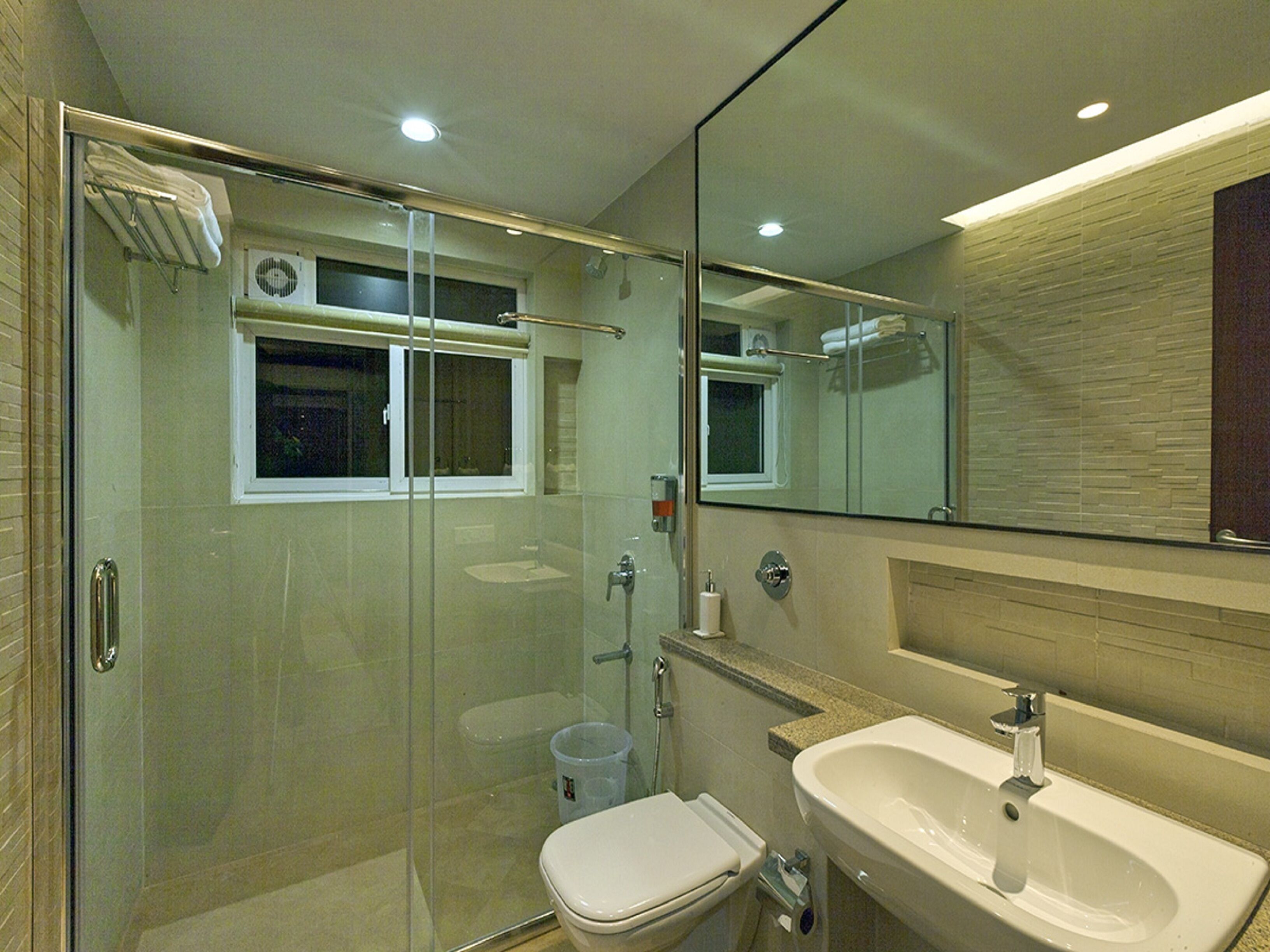 Un baño moderno con ducha de vidrio, inodoro blanco, lavabo y un espejo grande.