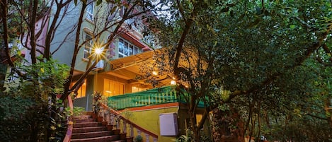 A staircase leading to a building with a green railing, surrounded by lush greenery.