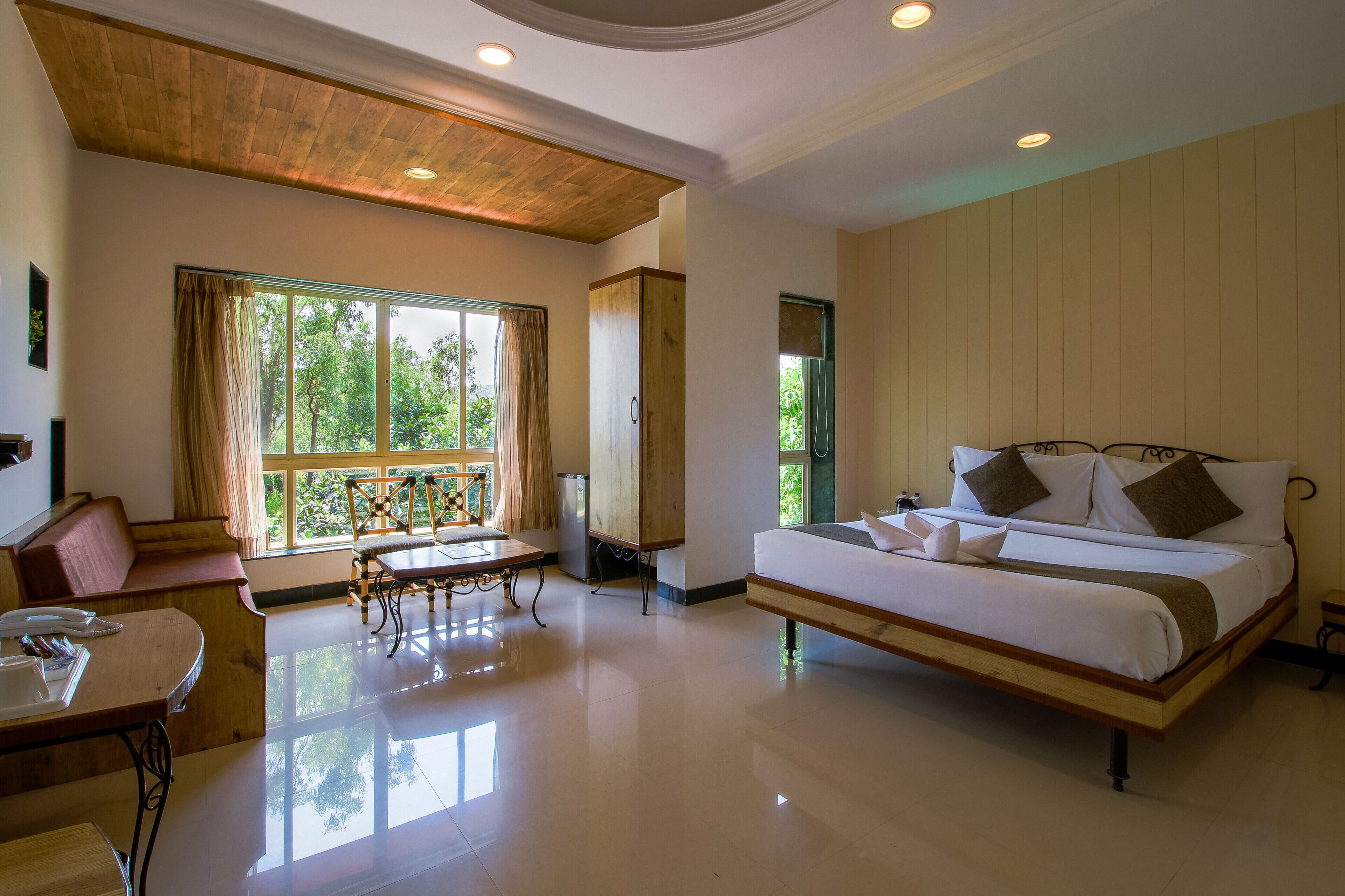 Un dormitorio espacioso con una cama grande, techo de madera, una mesa de comedor y vistas a zonas verdes por las ventanas.
