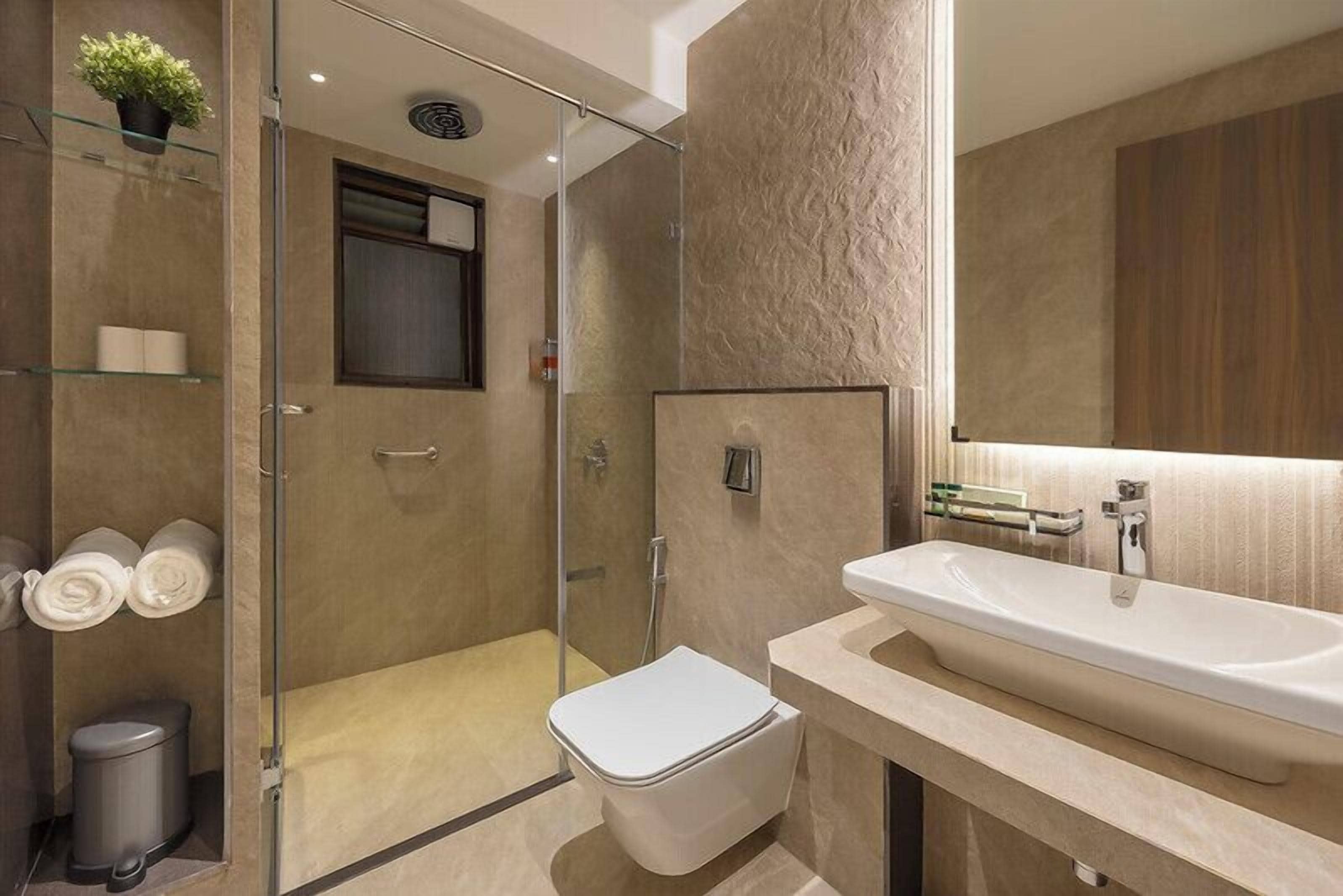 Een moderne badkamer met een douchecabine van glas, een wit toilet en een ruime wastafel met een spiegel erboven.