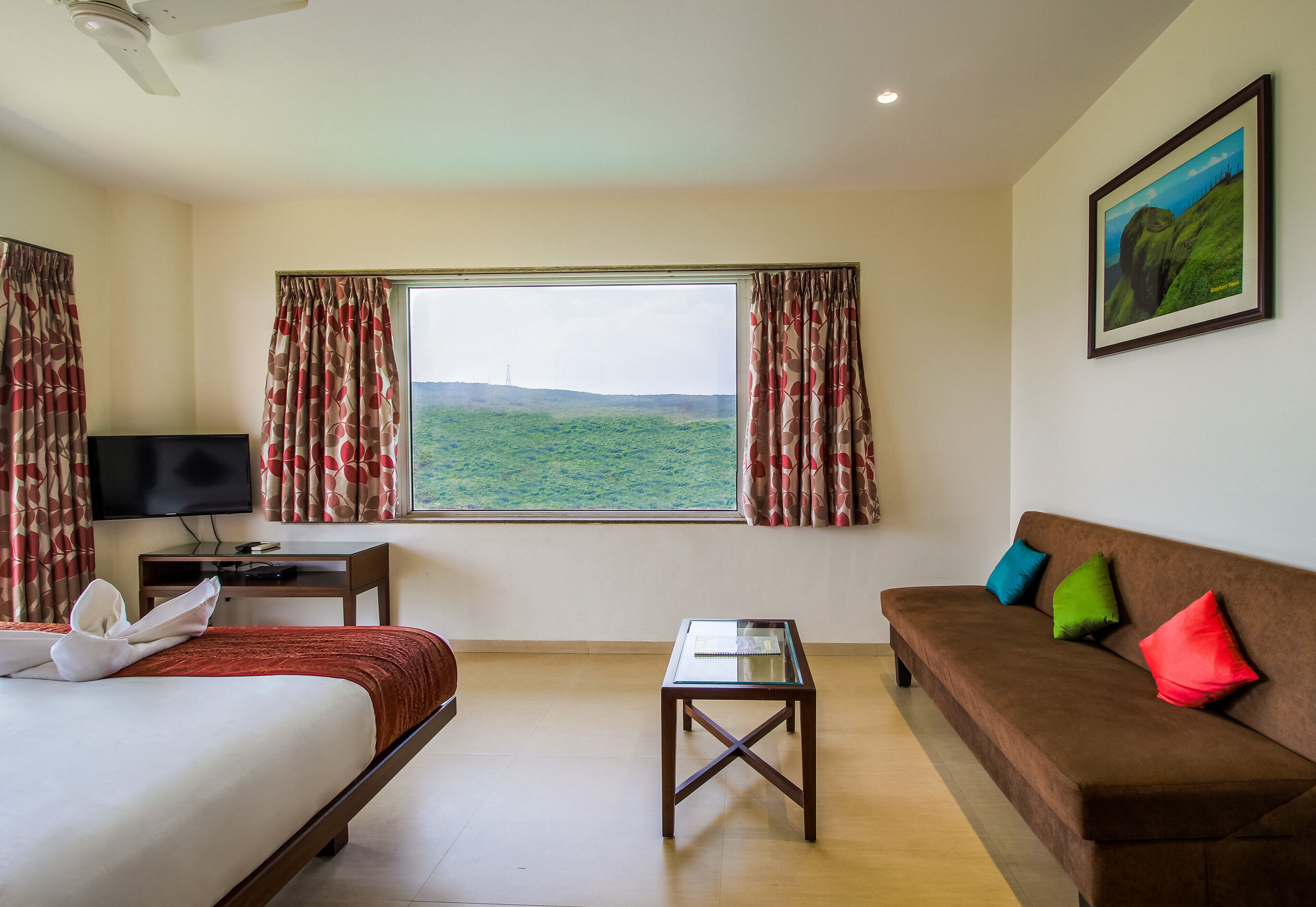 A hotel room with a bed, a sofa, a small table, a TV, and a window with curtains.