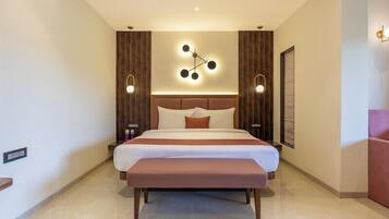 A modern hotel room with a large bed, a bench, and a wall-mounted light fixture.