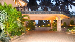 A hotel entrance with a covered walkway, palm trees, and stone pillars. - Wash and Wills Hotel (Mbale)
