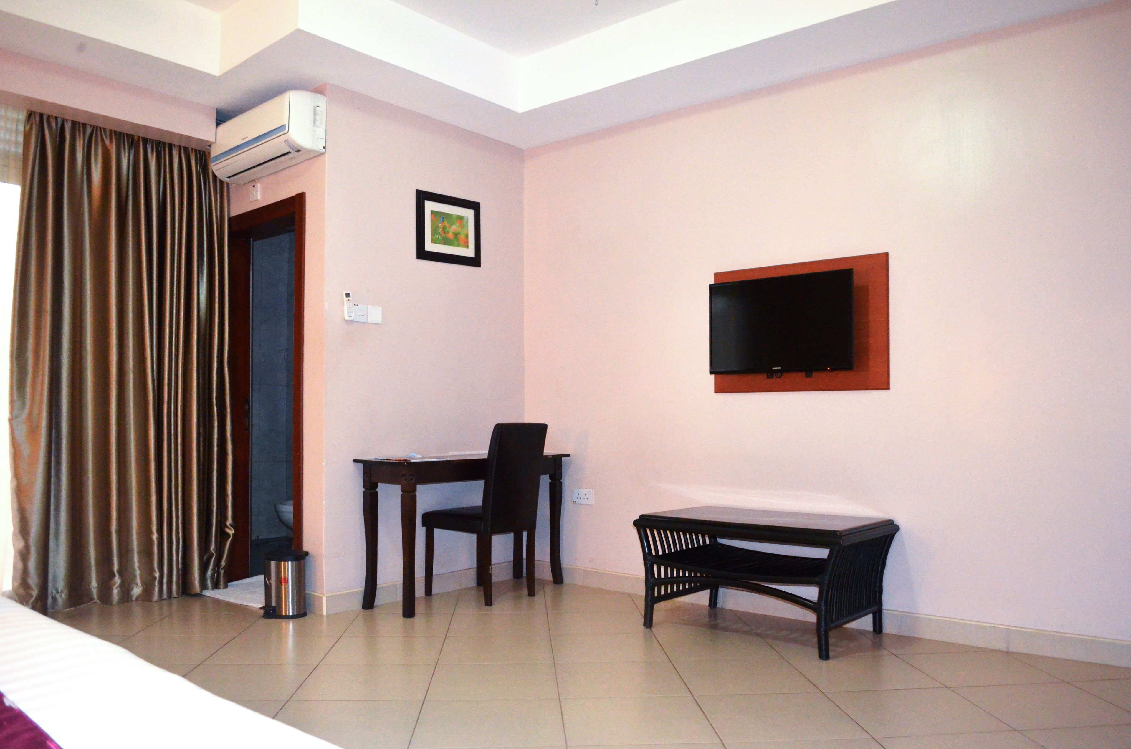 A hotel room with a bed, a desk, a chair, a TV mounted on the wall, and an air conditioning unit.