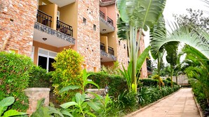 A multi-story building with brick and stone facades, balconies with metal railings, and a well-maintained garden with various plants and a paved walkway. - Wash and Wills Hotel (Mbale)