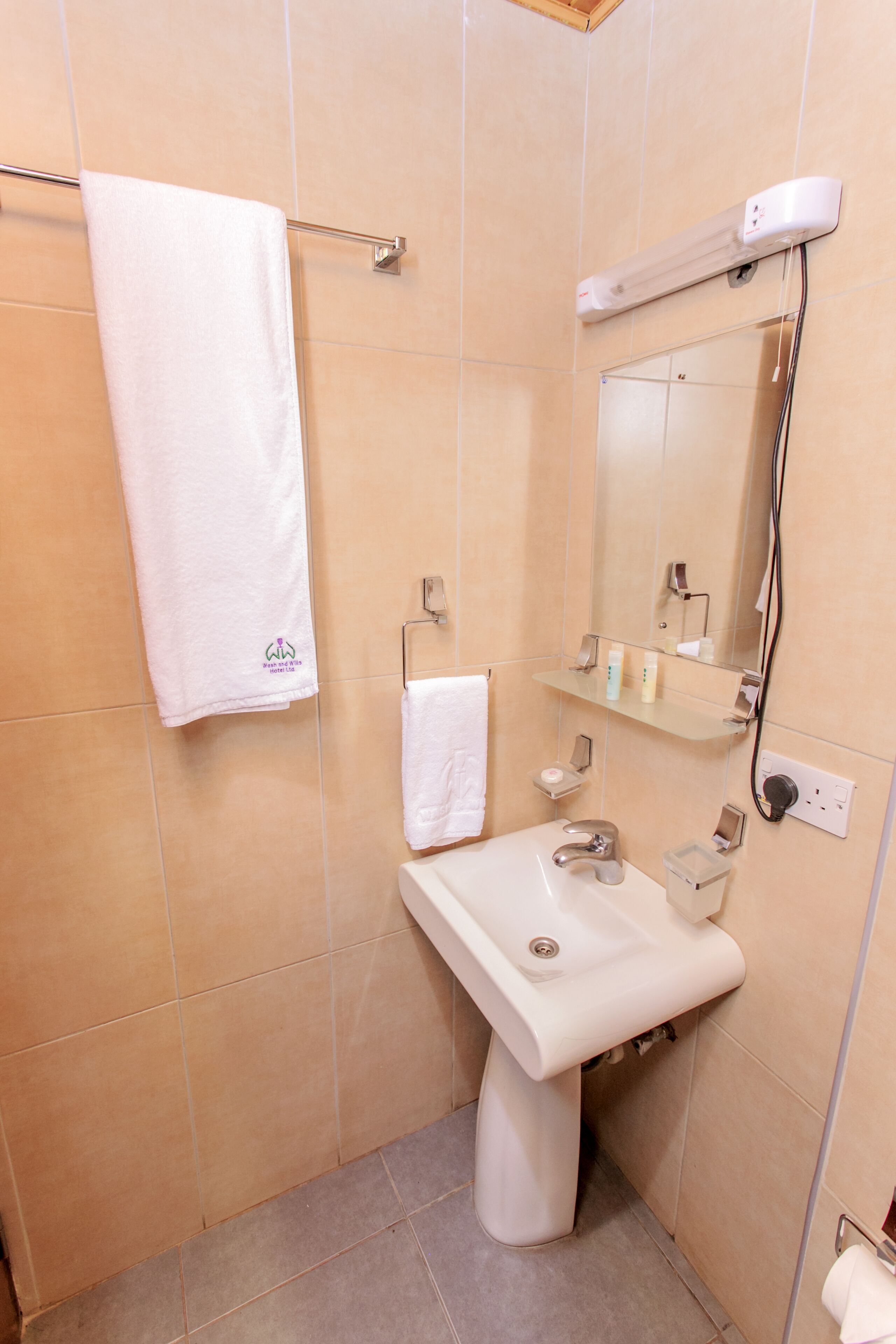 A bathroom with a white sink, a mirror, a towel rack, and a shelf with toiletries.