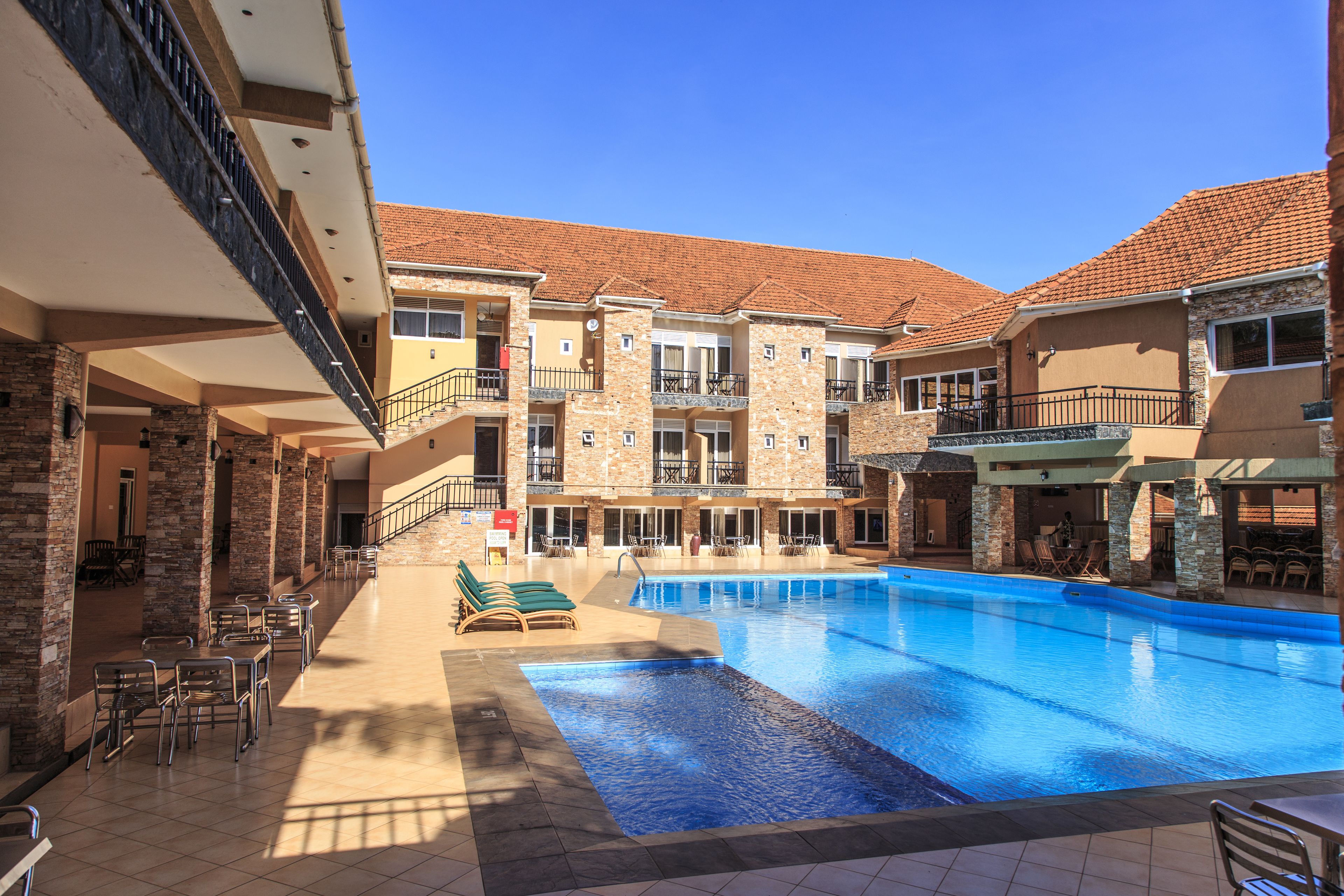 Un hotel con piscina, mobiliario exterior y un patio cubierto.