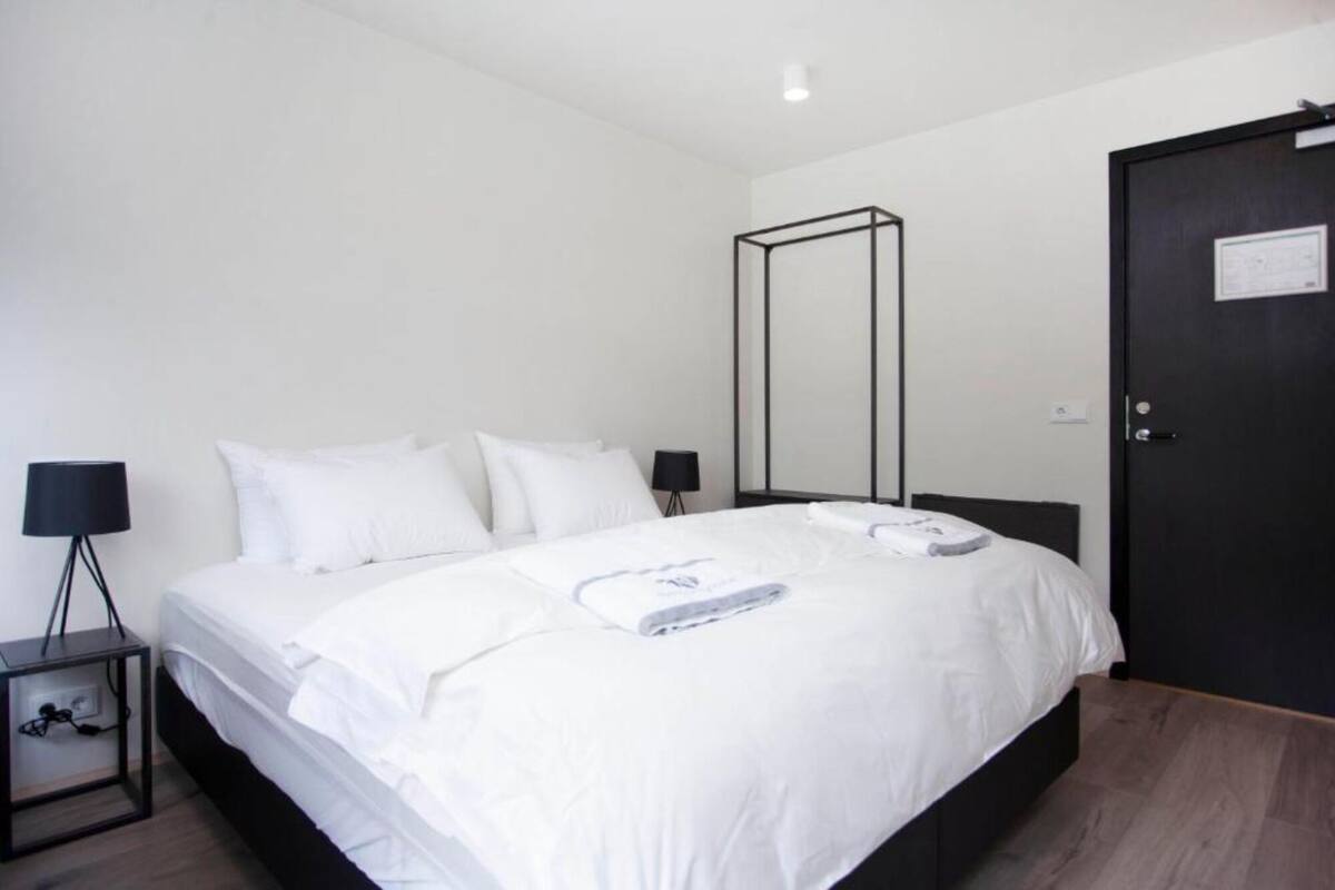 A modern hotel room with a large bed, two bedside tables with lamps, a wardrobe, and a mirror on the wall.