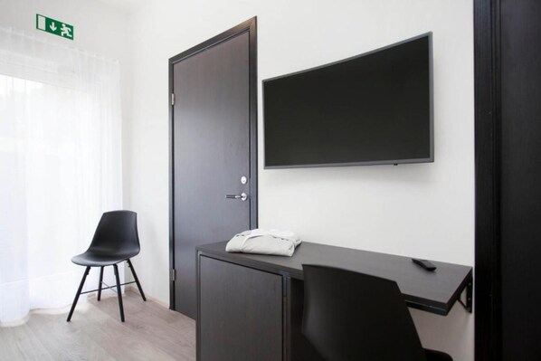 A hotel room with a desk, a chair, a wardrobe, and a flat-screen TV mounted on the wall.