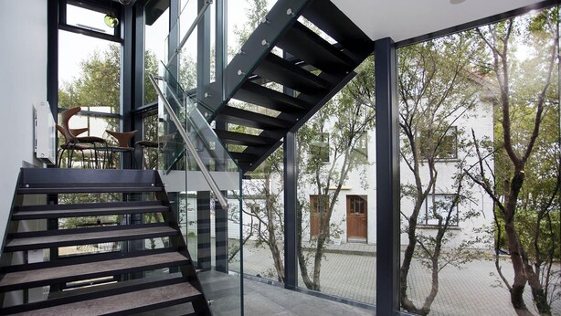 A modern staircase with glass railings leading to a balcony with a view of trees and a building. - Nordurey Hotel City Garden (Reykjavik)