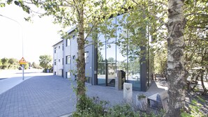 A modern building with a glass facade, a paved walkway, and a tree-lined entrance. - Nordurey Hotel City Garden (Reykjavik)