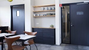 A modern dining area with tables and chairs, a kitchen counter with shelves, and a door labeled "ROOMS 101-103". - Nordurey Hotel City Garden (Reykjavik)
