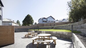 A patio area with wooden tables and benches, a stone wall, and a grassy lawn. - Nordurey Hotel City Garden (Reykjavik)