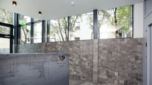 A reception area with a stone wall, a reception desk, and large windows overlooking trees. - Nordurey Hotel City Garden (Reykjavik)