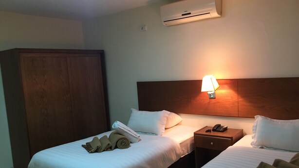 Ein Hotelzimmer mit zwei Betten, einem Kleiderschrank, einer Nachttischlampe und einer Klimaanlage.