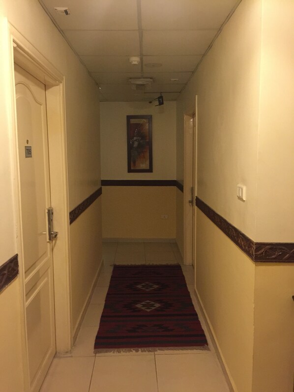 Un couloir avec un tapis à motifs, des murs blancs et une porte portant un numéro.