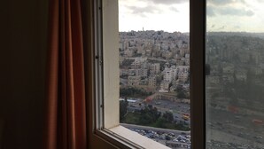 Ein Fenster mit Blick auf dicht bebautes Stadtgebiet, eine Straße mit Fahrzeugen und eine ferne Hügelkette mit Gebäuden.