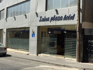 Enter the Zaina Plaza Hotel through its glass door with horizontal blinds.