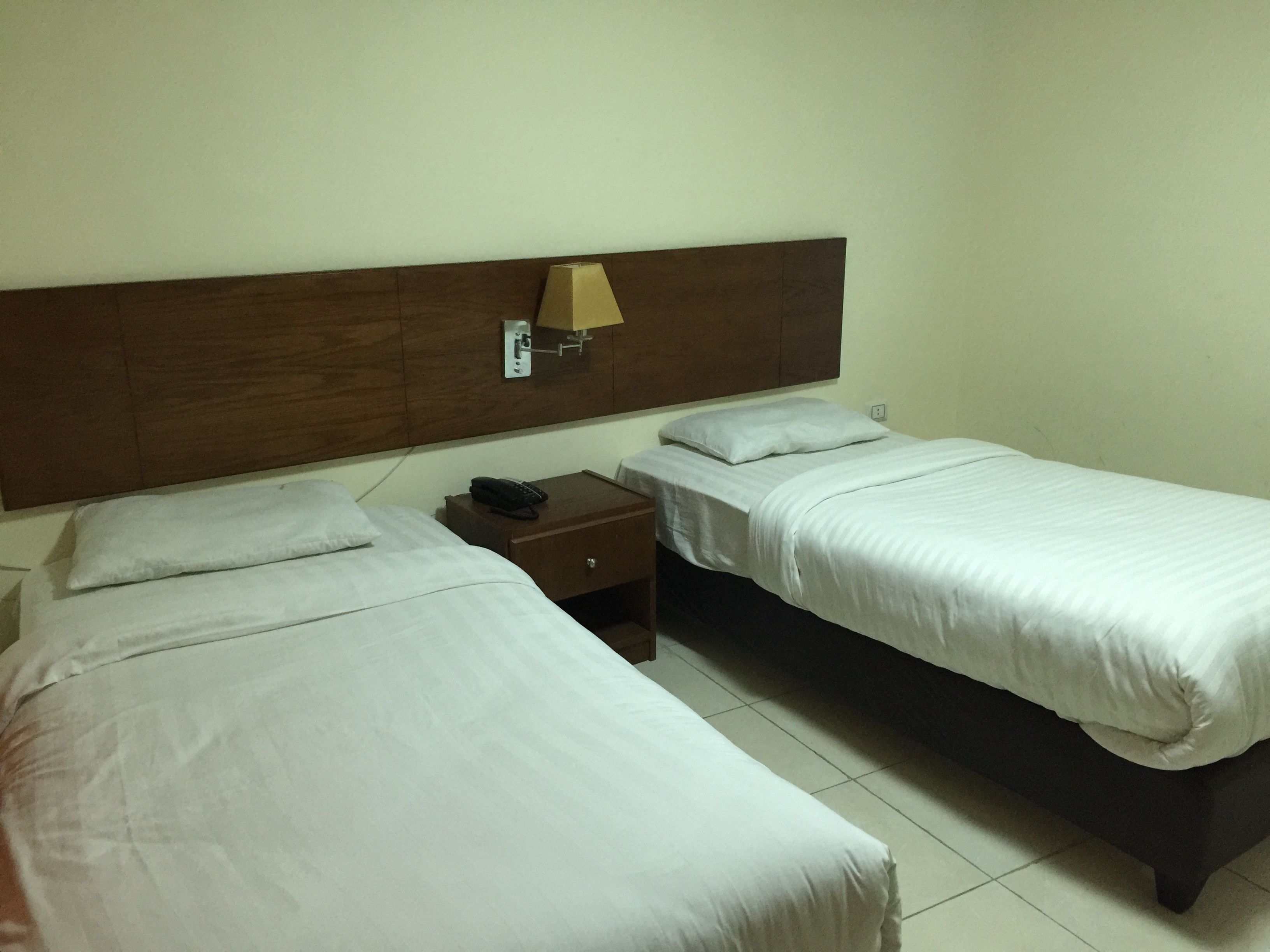 A hotel room with two single beds, a wooden headboard, a nightstand with a lamp, and a telephone.