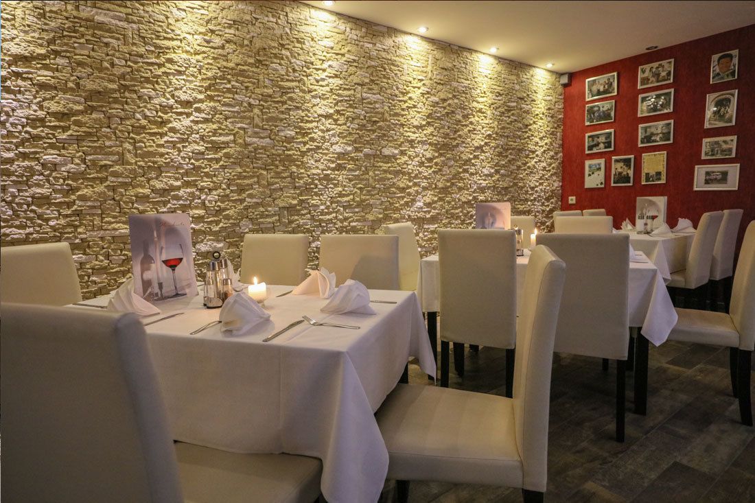 Un restaurant amb parets de pedra i teles de taula blanques. Les taules tenen posats caderots, draps de paper i coberts.