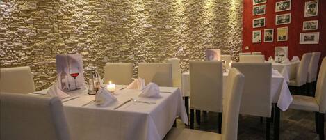 Un restaurant amb parets de pedra i teles de taula blanques. Les taules tenen posats caderots, draps de paper i coberts.