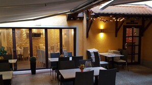 An outdoor dining area with tables and chairs, a glass door entrance, and a building with a tiled roof. - Hotel Restaurant Zur Traube (Freyburg)