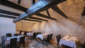 A restaurant with a rustic stone wall and exposed wooden beams. Tables are set with white tablecloths and chairs. - Hotel Restaurant Zur Traube (Freyburg)