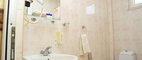 A bathroom with a sink, toilet, and a hairdryer on a shelf.