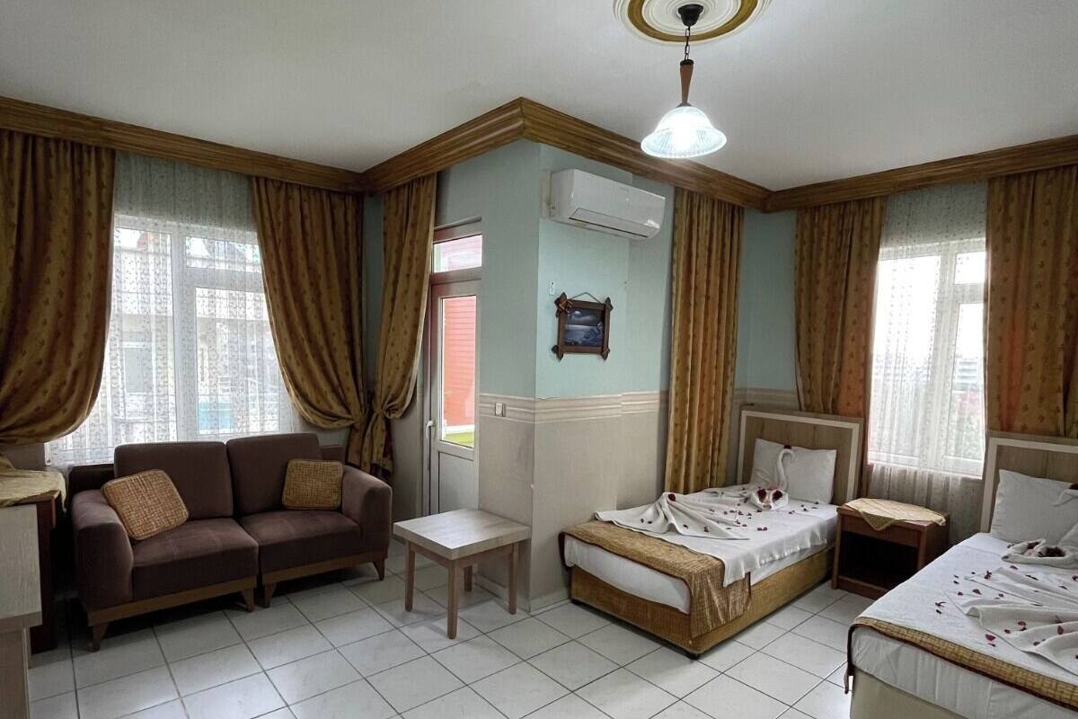 A room with a sofa, two single beds, a small table, and an air conditioning unit.