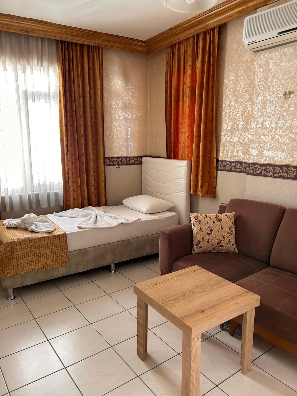 Un ambiente compatto con un letto, una divano, un tavolino e una finestra con tende.